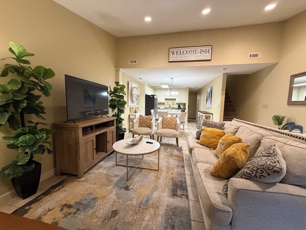 A living room with a television, a sofa, a coffee table, and a 'WELCOME-ISH' sign.