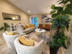 A living room with a sofa, armchairs, a coffee table, a bookshelf, and a large plant.