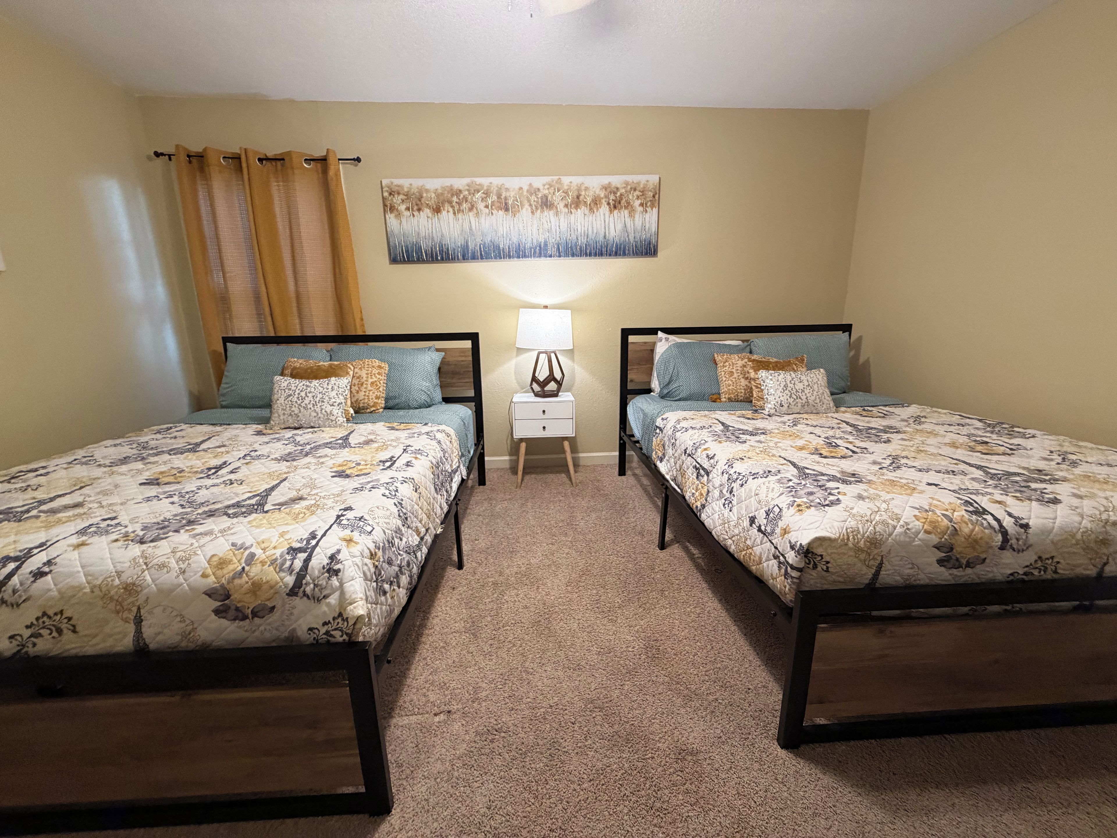 A bedroom with two beds, a nightstand, a lamp, and a painting on the wall.