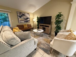 A living room with a sofa, armchair, TV stand, and a painting on the wall.