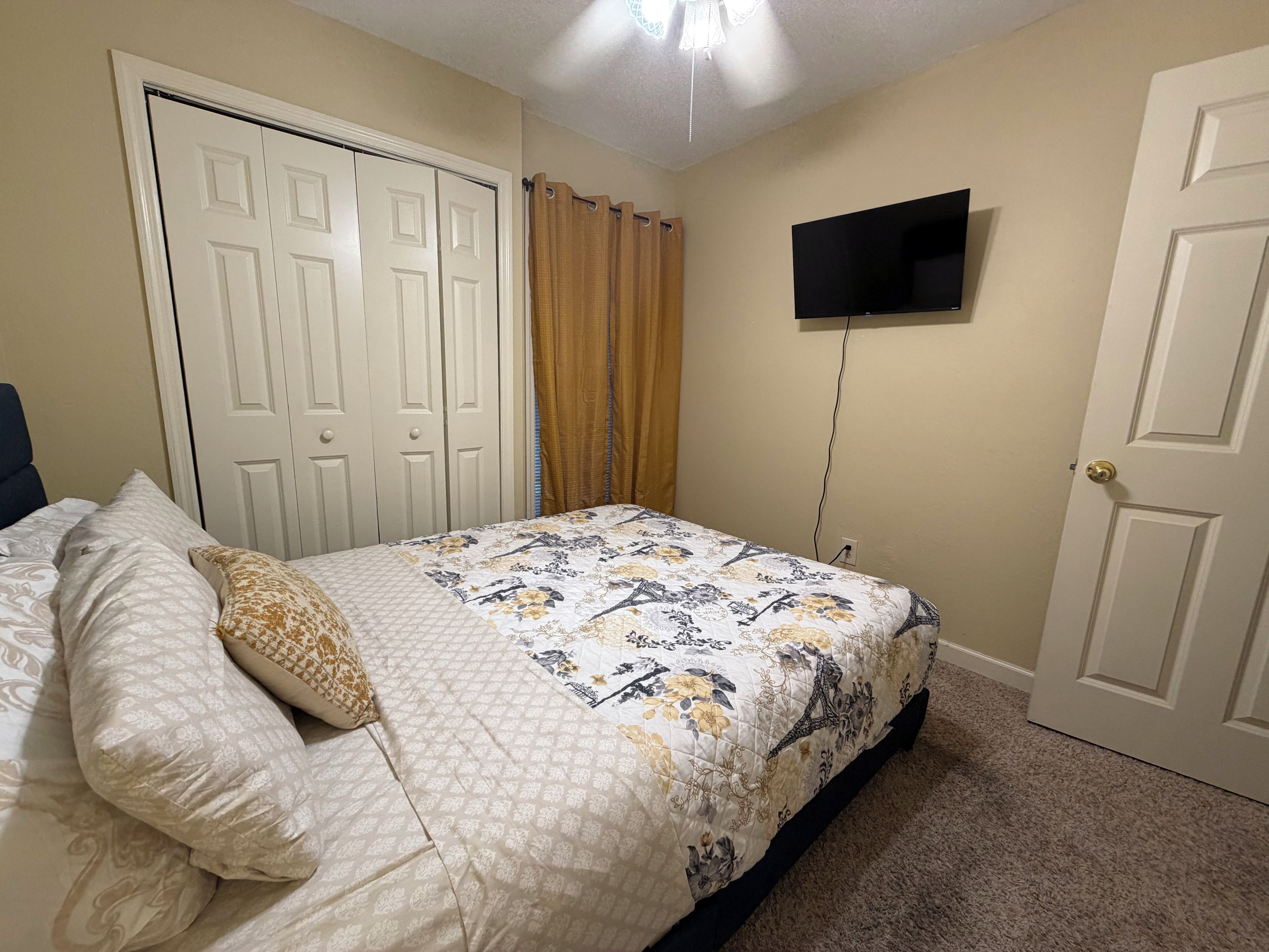 A bedroom with a bed, a television mounted on the wall, and a door.