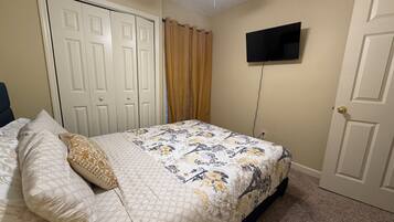 A bedroom with a bed, a television mounted on the wall, and a door.