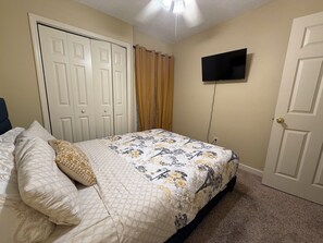A bedroom with a bed, a television mounted on the wall, and a door.