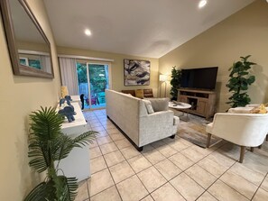 A living room with a sofa, armchairs, a coffee table, a TV, and a plant.