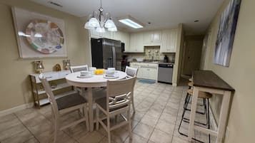 Uma cozinha moderna com armários brancos, uma mesa de jantar com cadeiras, uma geladeira e uma lava-louças.