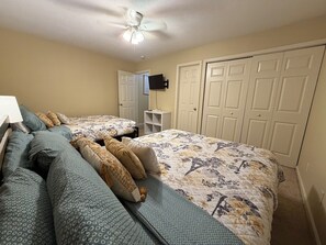 A bedroom with two beds, a ceiling fan, a TV, and a wardrobe.
