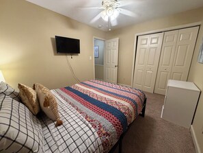 A bedroom with a bed, a television, a ceiling fan, and a wardrobe.