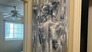 Un couloir orné d’un tableau représentant une femme, avec un ventilateur de plafond et un lit visible au fond.