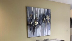 Une cuisine avec un comptoir blanc, trois tabourets de bar et un grand tableau abstrait accroché au mur.