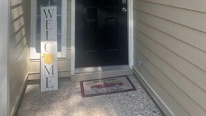Une entrée de maison avec une pancarte « BIENVENUE », un paillasson orné d’une voiture et de l’inscription « Bienvenue chez nous », et le numéro de la maison, 2113.