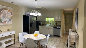 Une cuisine moderne avec des meubles blancs, un réfrigérateur en acier inoxydable et un coin repas comprenant une table ronde et des chaises.