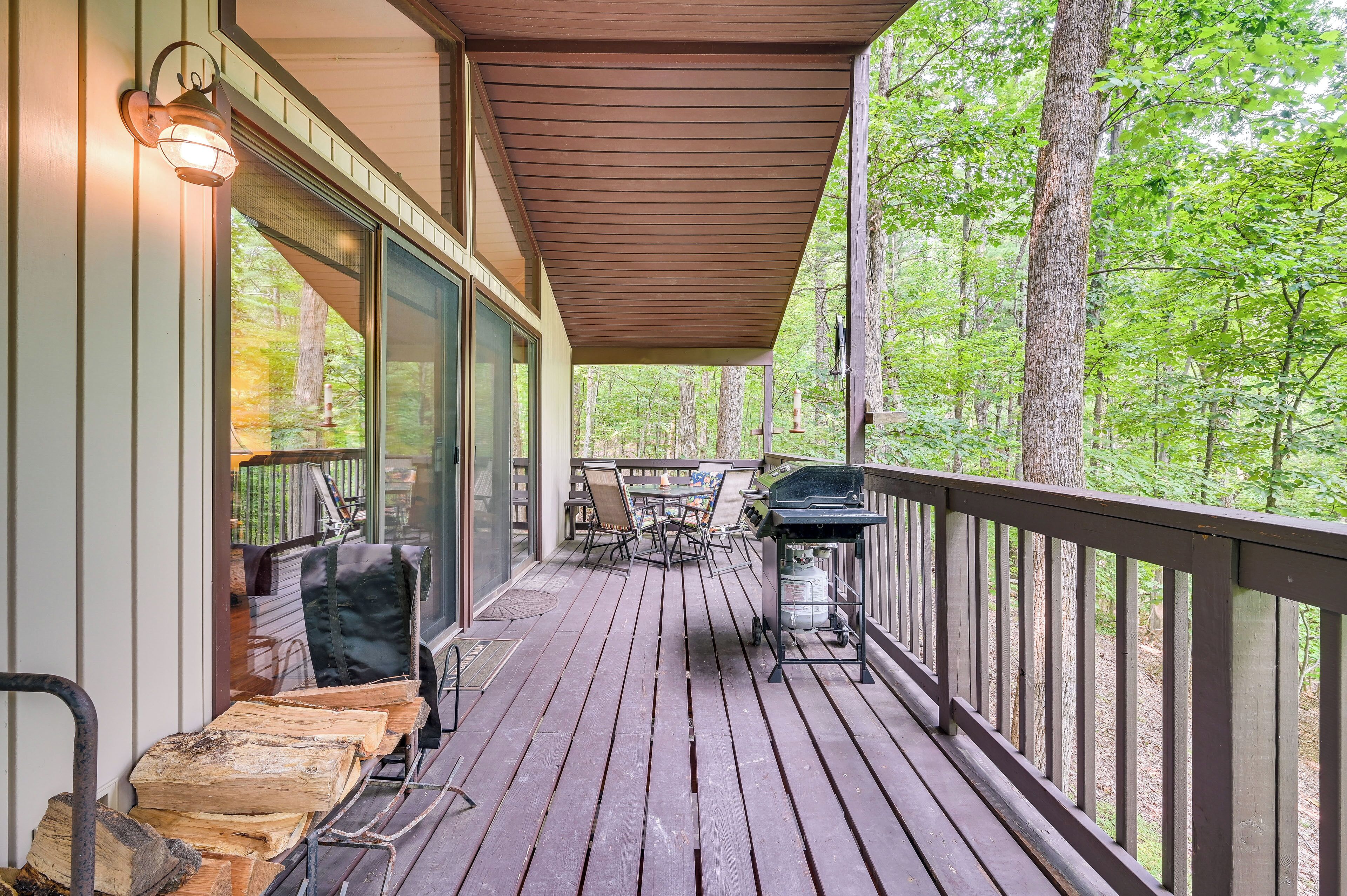 A covered deck with a grill, outdoor furniture, and a view of the forest.