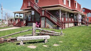 A red two-story building with a porch and a staircase leading to the upper floor. - Auberge Akamaraska (Kamouraska)