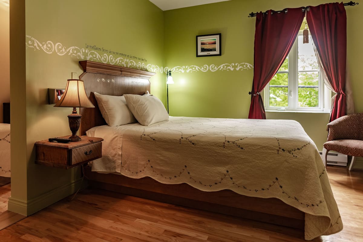 A bedroom with a bed, bedside table, lamp, and a window with curtains.