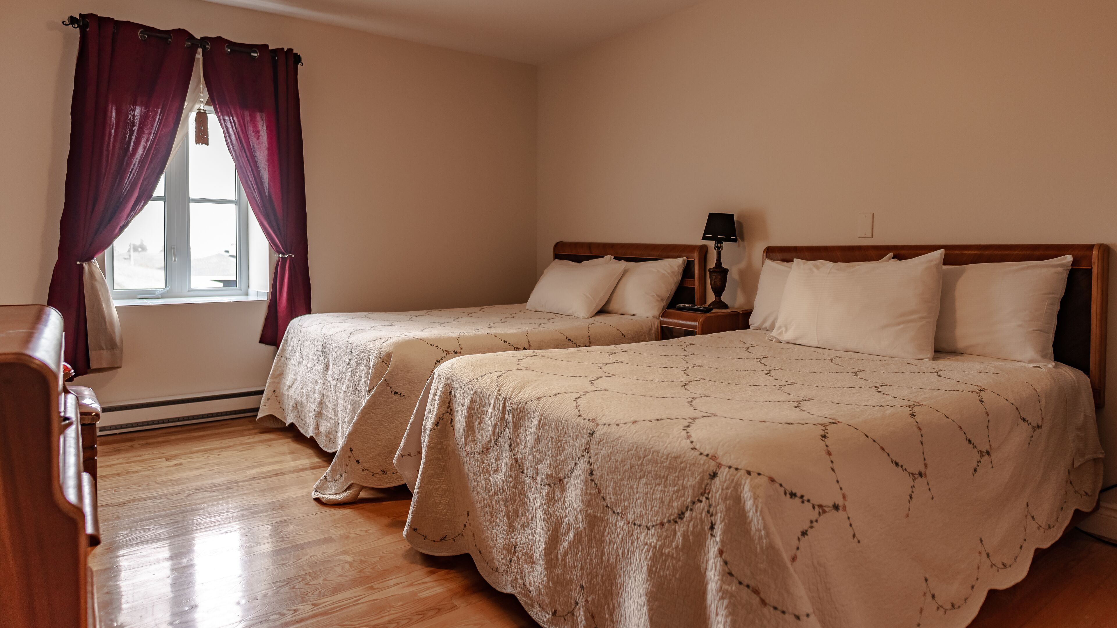 Habitación de hotel con dos camas, una mesita de noche con lámpara, cómoda de madera y ventana con cortinas.