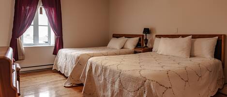 Habitación de hotel con dos camas, una mesita de noche con lámpara, cómoda de madera y ventana con cortinas.