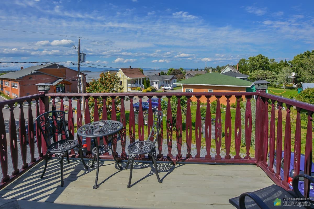 A balcony with a red railing, two metal tables, and chairs.