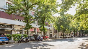 A street lined with parked vehicles and trees, with buildings featuring storefronts and balconies. - GuestHost - Verona Central Apartment with Balconies! (Verona)