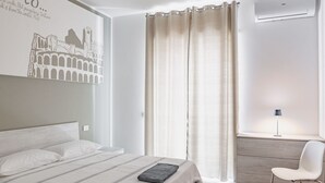 A bedroom with a bed, a desk, a chair, a wall-mounted air conditioner, and a curtain. - GuestHost - Verona Central Apartment with Balconies! (Verona)