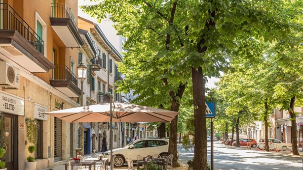 Outdoor seating with umbrellas, a parked car, and a street lined with buildings. - GuestHost - Verona Central Apartment with Balconies! (Verona)