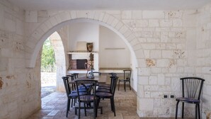 Un interior con paredes de piedra, chimenea de ladrillo y zona de comedor con sillas y mesa.