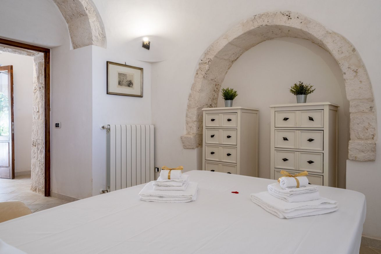 Un dormitorio con una cama grande, dos cómodas blancas, un radiador y una pared de piedra con arco.