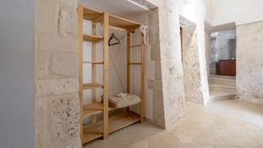 Una habitación con pared de piedra, una estantería de madera y una escalera que conduce a otra zona.