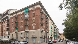 A multi-story building with balconies, a pedestrian crossing, and parked cars. - GuestHost - Functional apartment perfect for 4 guests located in a strategic and well-served position, in the heart of the Lingotto area, ideal for work, tourism and study. We are just a few minutes from the hospital area (Molinette, San Lazzaro Dermatol (Torino)