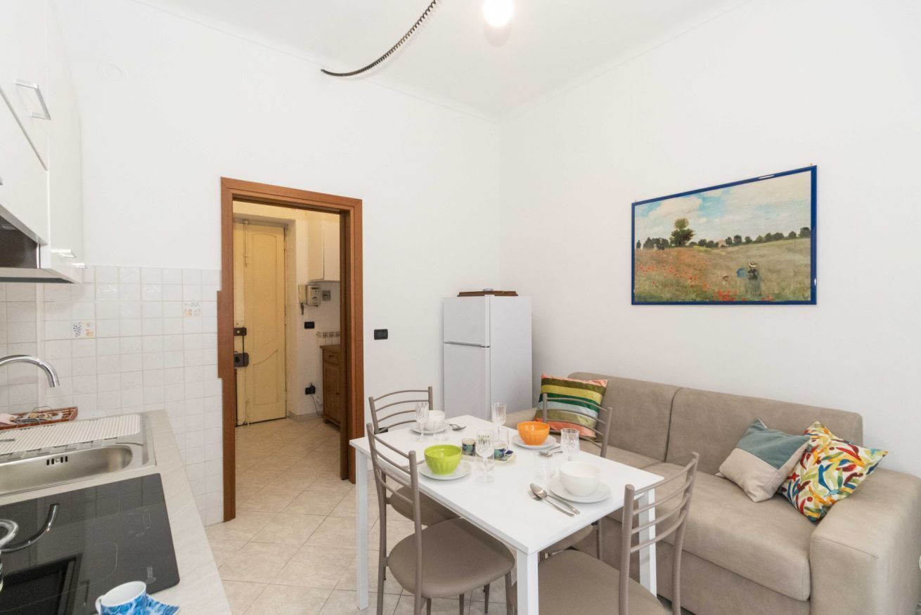 A compact kitchen with a dining table, chairs, a sofa, and a painting on the wall.