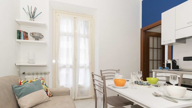 A compact living space with a sofa, dining table, chairs, a kitchen area, and a door with a window. - GuestHost - Functional apartment perfect for 4 guests located in a strategic and well-served position, in the heart of the Lingotto area, ideal for work, tourism and study. We are just a few minutes from the hospital area (Molinette, San Lazzaro Dermatol (Torino)