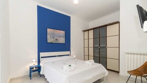 A bedroom with a bed, a nightstand, a blue wall, a painting, a wardrobe, and a chair. - GuestHost - Functional apartment perfect for 4 guests located in a strategic and well-served position, in the heart of the Lingotto area, ideal for work, tourism and study. We are just a few minutes from the hospital area (Molinette, San Lazzaro Dermatol (Torino)