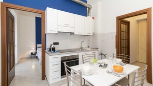 A compact kitchen with white cabinets, a built-in oven, and a dining area with a table set for two. - GuestHost - Functional apartment perfect for 4 guests located in a strategic and well-served position, in the heart of the Lingotto area, ideal for work, tourism and study. We are just a few minutes from the hospital area (Molinette, San Lazzaro Dermatol (Torino)