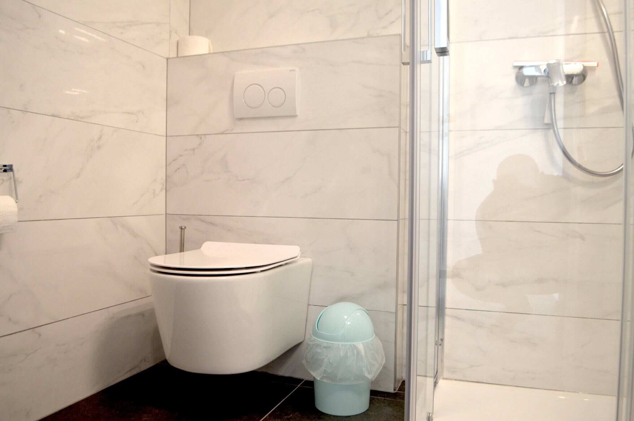 A bathroom with a toilet, a shower, and a trash bin.
