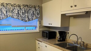 A compact kitchen with white cabinets, a microwave, a sink, and a window with a patterned curtain. - Cozy house ON the ATV/ORV trail located in Newberry.  Great for year round fun.  (Newberry)