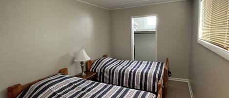 A bedroom with two beds, a ceiling light, and a window with blinds.