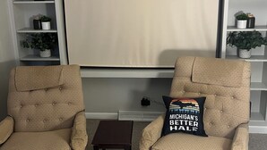 A room with two beige armchairs, a small table, and a bookshelf with decorative items. - Cozy house ON the ATV/ORV trail located in Newberry.  Great for year round fun.  (Newberry)