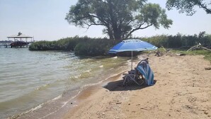 Een strand met een blauwe parasol, een beschaduwd zitgedeelte en een steiger met een boot.