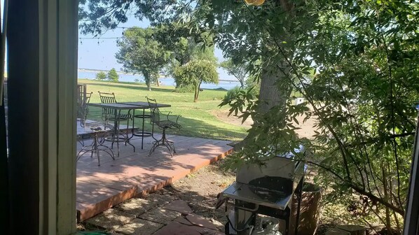 A patio with a table and chairs, a barbecue grill, and a view of a grassy area and water. - Go jump in the Lake-Ray Hubbard (Rowlett)