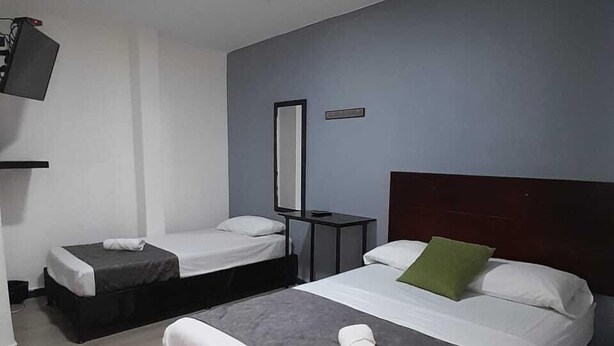 Quarto de hotel com duas camas de solteiro, uma cama grande, uma TV de tela plana e uma mesinha.