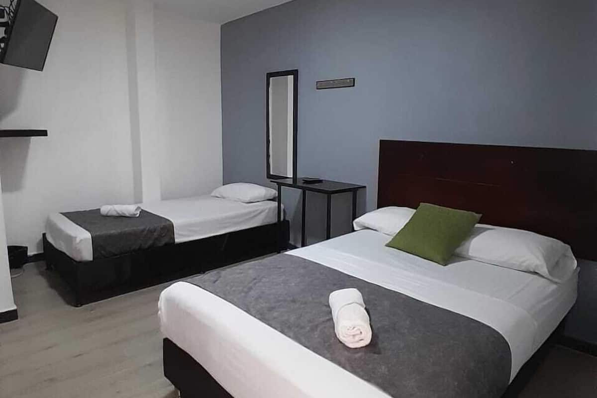 A hotel room with two single beds, a large bed, a flat-screen TV, and a small table.