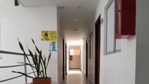 Um corredor comprido e estreito com paredes brancas, chão de azulejos e um vaso de planta à esquerda.