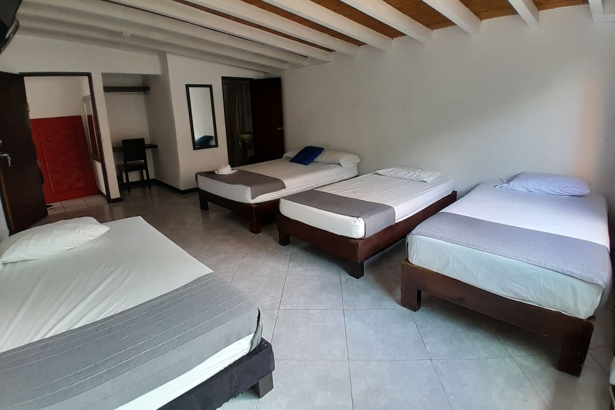 A hotel room with three beds, a wooden ceiling, and a red door.