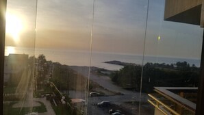 A view through a window with a sunset, a parking area, and a road leading to a body of water. - Chalet In Solemar, Generator is Included, Parking, Wifi (Jounieh)