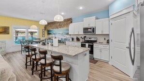 Una cocina moderna con armarios blancos, una isla grande con taburetes de bar, un microondas y un refrigerador.