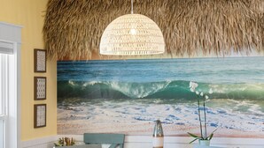 Un comedor con mesa y sillas de madera, techo de paja y un amplio mural marino en la pared.