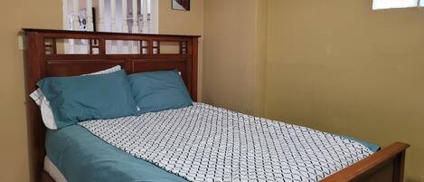 Un dormitorio con estructura de cama de madera, ropa de cama color turquesa y colcha estampada.