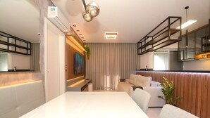 Ein modernes Wohnzimmer mit Esstisch in Weiß, einer Couch und einer Küchenzeile mit einer Wand in Holzoptik.