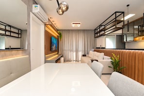 Una sala de estar moderna con una mesa de comedor blanca, un sofá y una zona de cocina con horno empotrado.