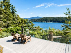 A deck with wooden chairs and a glass balustrade overlooking a lake and forest. - Waterfront Room with Private Bath and Deck Near Marina, Private Beach Access (Gibsons)