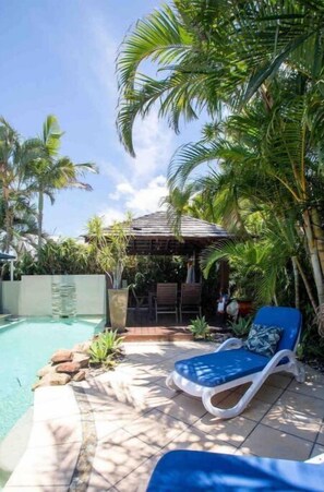 Relax by the pool surrounded by lush greenery and a shaded seating area.